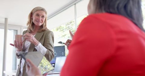 Professional older female manager chats with team in modern workspace