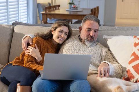 Couple cuddling on couch sharing laptop with dog in cozy knit sweaters