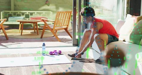 Man tying running shoes at sunlit patio doorway preparing for home workout with dumbbells