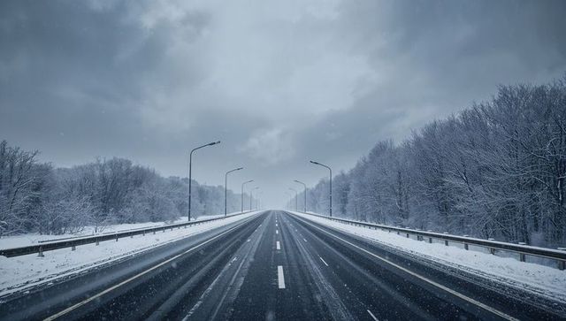 Empty snowy highway stretching into foggy winter forest with wet tire tracks