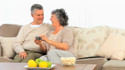 Smiling Senior Couple Enjoying Moments on Sofa with Camera