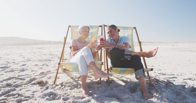 Senior couple enjoying a relaxing moment on the beach, sitting in deck chairs and toasting with colorful drinks. Useful for themes around retirement planning, leisure vacations, healthy lifestyles, and relationships in older age. Perfect for advertisements, brochures and online content focusing on senior lifestyle, travel, and happiness.