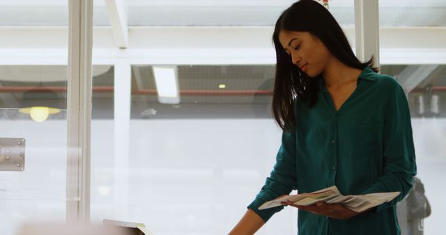 Young biracial woman in an office setting, reviewing documents. She appears focused on her work, exemplifying professionalism and dedication.