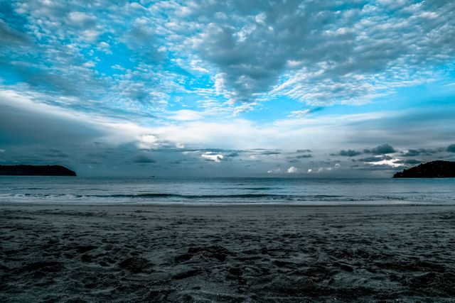 Calm beach scene at dusk with dramatic blue sky filled with wispy clouds. Perfect for use in travel brochures, nature websites, relaxation and meditation content, or background images in presentations.