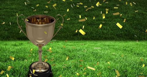 Gold trophy and falling confetti celebrating victory on sports stadium grass