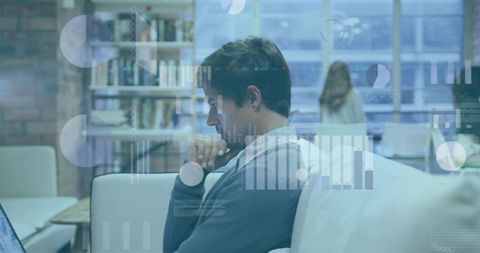 Young professional working on laptop in coworking lounge with data visualization overlay
