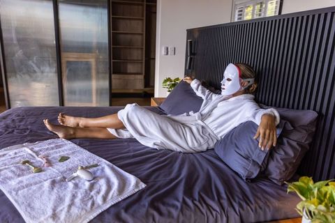 Woman relaxing on bed wearing led facial mask and bathrobe for at-home skincare