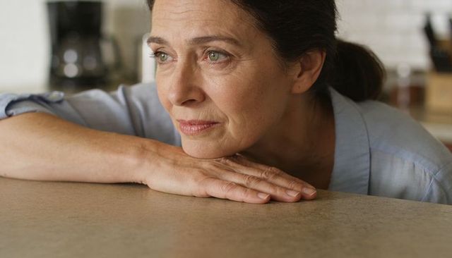 Contemplative mature woman leaning on kitchen counter, serene domestic morning portrait