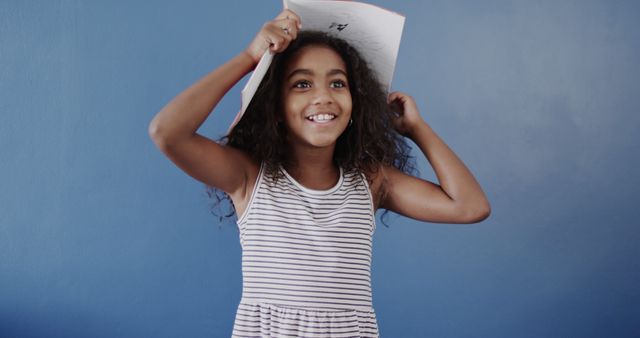 Cheerful Girl Holding Notebook on Head Against Blue Background - Download Free Stock Images Pikwizard.com