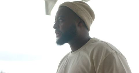 Contemplating african man wearing beige beanie on veranda high-key minimal serene portrait