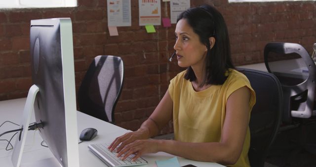 Biracial businesswoman wearing headset sitting at desk using computer. business in a modern office.