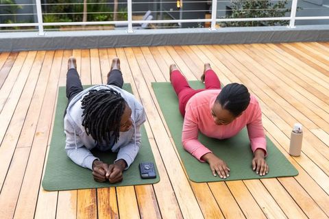 African american friends doing rooftop stretching workout on wooden deck with yoga mats