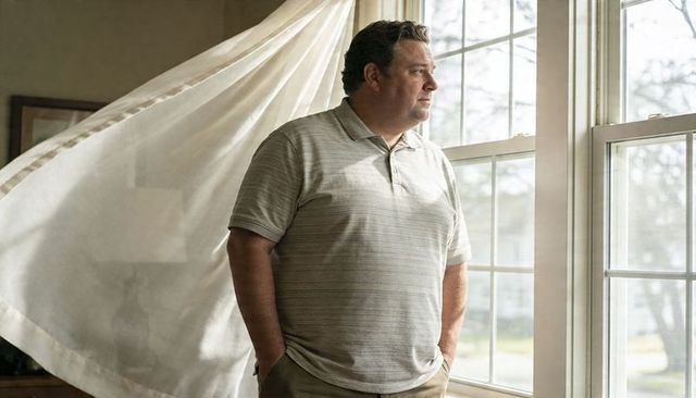 Man gazing through sunlit window with billowing sheer curtain, contemplative home moment