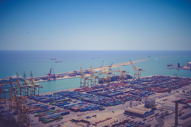 Aerial view of a bustling cargo port with numerous shipping containers and cranes alongside the sea. Ideal for illustrating global trade, import-export business, logistics industry, and maritime transportation. Useful for articles on commerce, shipping industry reports, logistics and supply chain analysis, port operations, and industrial activities.
