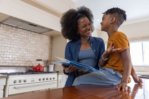 African american mother reading picture book with smiling son on cozy kitchen island