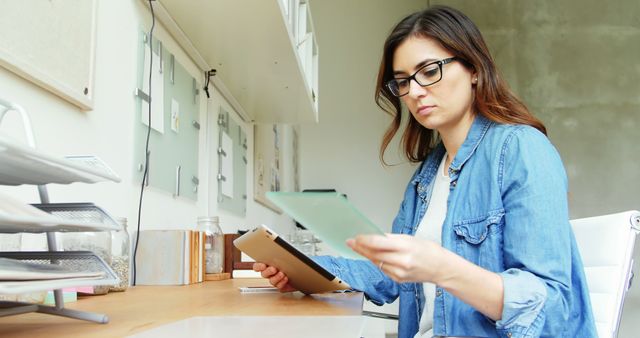 Focused Young Woman Reading Documents at Modern Office Desk - Download Free Stock Images Pikwizard.com