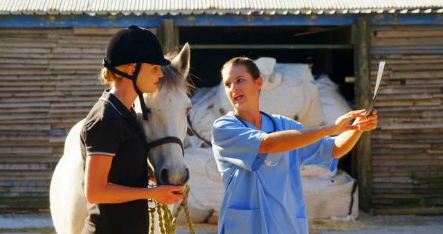 Veterinarian in blue scrubs explains treatment to young horse rider on rural farm. Ideal for themes including animal care, veterinary services, rural lifestyle, equestrian activities, and farm life.