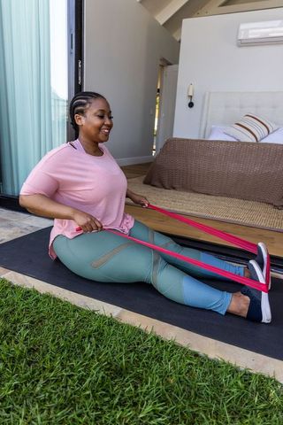 African american woman exercising with pink resistance band at bedroom doorway for home workout