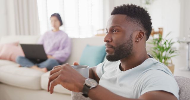 Thoughtful man drinking coffee while sitting on sofa at home - Download Free Stock Images Pikwizard.com