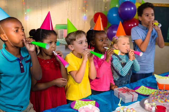 Children enjoying a birthday party, wearing colorful party hats and blowing party horns. Ideal for use in advertisements, birthday invitations, party planning websites, and children's event promotions.