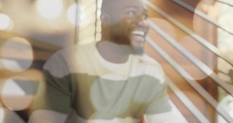 Laughing man on wooden staircase with warm bokeh lights, cozy striped sweater