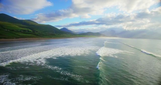 Beautiful aerial scene of waves gently washing onto serene coastline, green hills and mountains in background. Ideal for travel websites, nature blogs, and landscape-oriented publications.