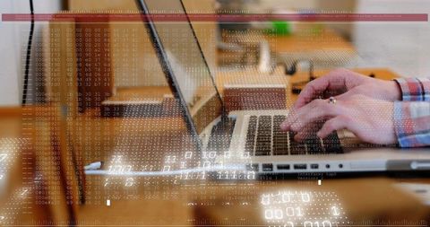Hands typing on laptop with code overlay reflecting on wooden desk for tech workflow