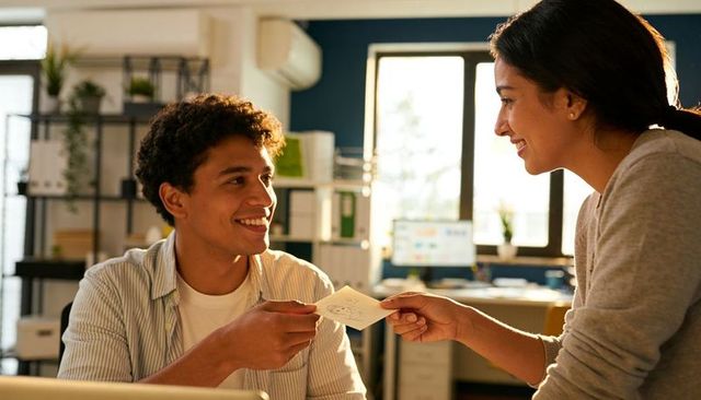 Coworkers exchanging note while smiling and collaborating in sunlit modern office workspace