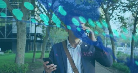 Urban commuter walking and sipping travel mug while checking smartphone with teal bokeh