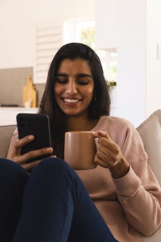 Young Asian Woman Relaxing with Smartphone and Mug in Modern Apartment