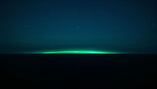 Emerald aurora band glowing along remote night horizon over dark flat expanse minimal