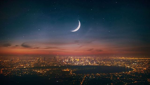Crescent moon over coastal city skyline at dusk