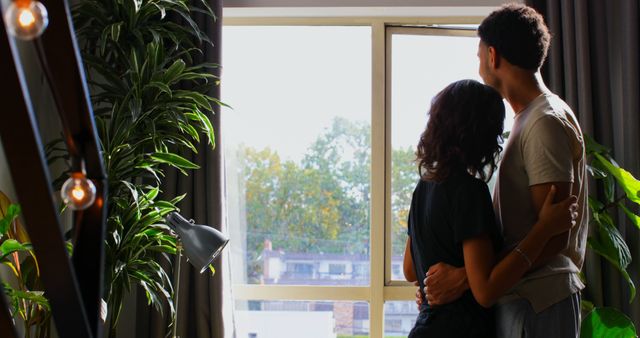 Couple Embracing and Looking Out Window in Cozy Apartment - Download Free Stock Images Pikwizard.com