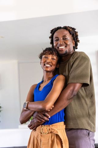 African american couple hugging and smiling at home wearing smartwatch and casual clothes