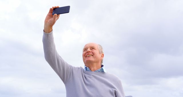 Happy senior caucasian man using smartphone and taking pictures on beach. Retirement, communication, summer, leisure, vacation and senior lifestyle, unaltered.