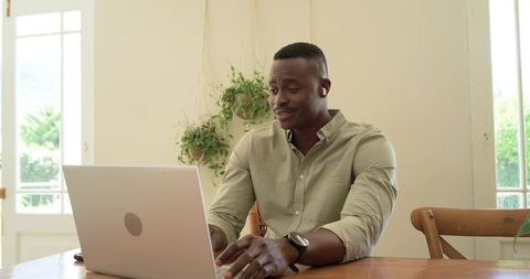 African american man working remotely on laptop in sunlit minimalist home office