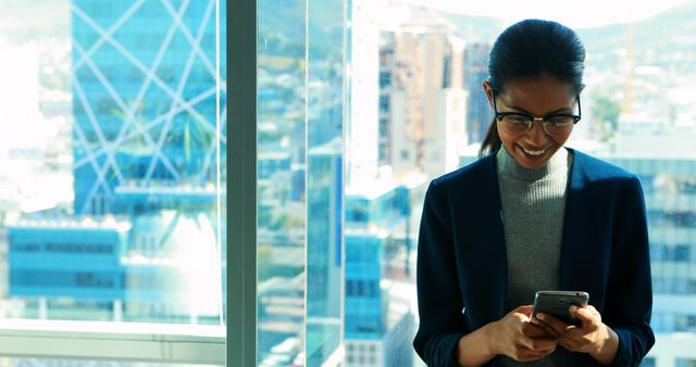 Businesswoman Using Smartphone Near Office Window in Urban Environment - Download Free Stock Images Pikwizard.com