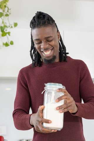 Smiling african american man holding clamp-top jar of flour preparing to bake in bright kitchen