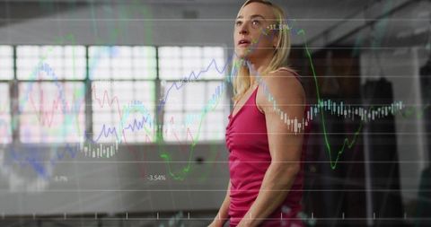 Female athlete studying financial charts while training in studio gym with data overlay
