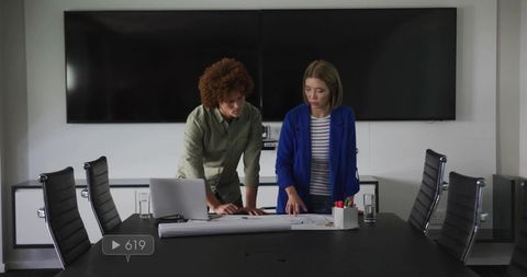 Business Architects Collaborating over Blueprints in Modern Boardroom with Laptop Screens