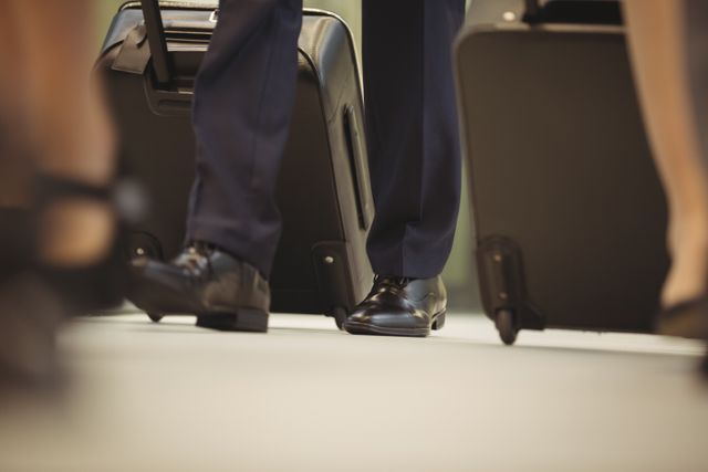 Low angle view of a businessman in a suit walking with a trolley bag. Ideal for use in travel-related content, business travel articles, airport services promotions, and professional commuting themes.