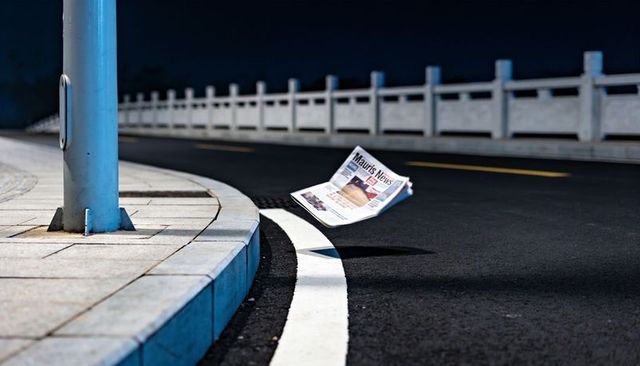 Floating newspaper hovering above curved urban road at night with dramatic streetlight shadow