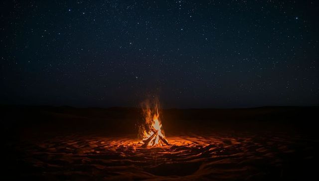 Desert bonfire under starry sky casting warm glow on rippled sand