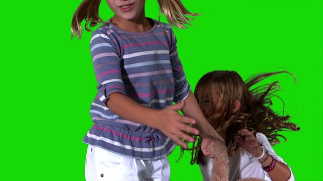 Two young sisters are seen jumping and playing with a teddy bear with a green screen background. They are wearing casual clothes and experiencing joy and togetherness. Perfect for use in projects depicting family life, childhood joy, playful moments, or promotional materials for children's products.