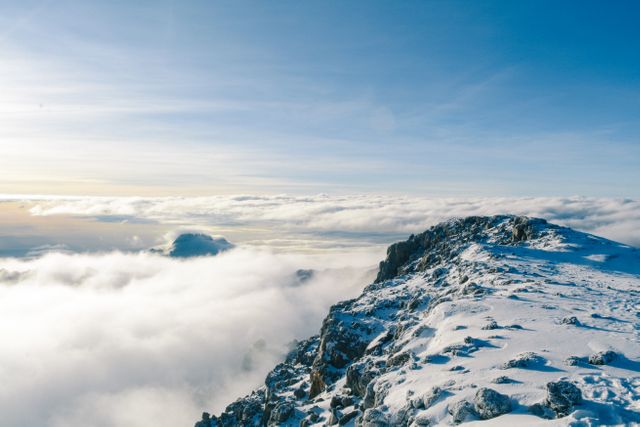 Snow-covered mountain peak bathed in sunlight with a sea of clouds below, creating a striking natural landscape. Ideal for promotions and content related to winter travel, outdoor adventures, climbing, scenic beauty, and natural landscapes.