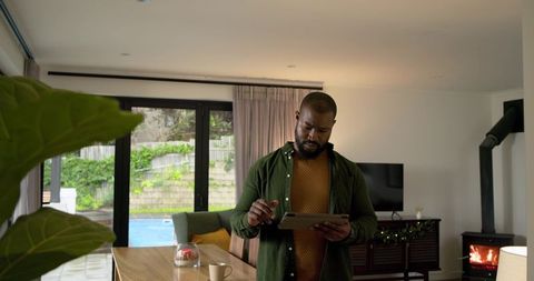 African American man using tablet with stylus in modern lounge overlooking backyard pool