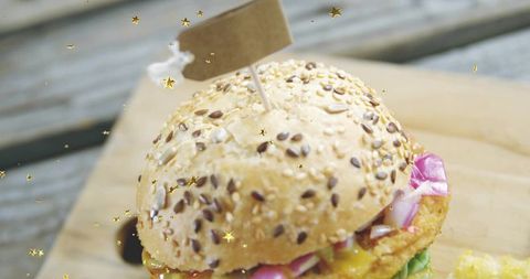 Seeded bun crispy patty burger with red onion, greens and gold confetti closeup