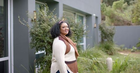 African American woman smiling in modern front yard wearing knit sweater and rust scarf