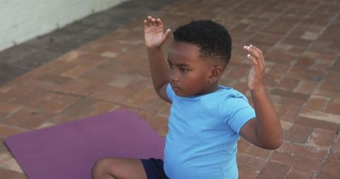 Young boy practicing yoga on patio mat raising arms during outdoor stretching session