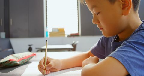 Focused Asian Schoolboy Writing at Desk in Classroom Setting - Download Free Stock Images Pikwizard.com